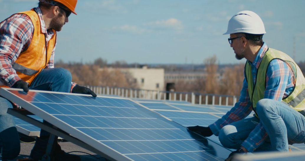 Two construction workers installing a solar panel on a rooftop.