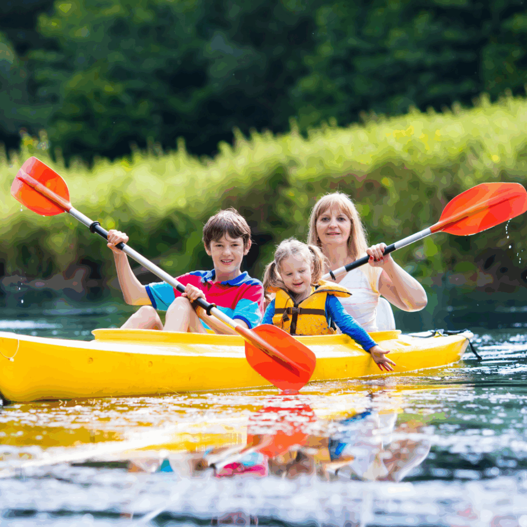 Family of three kayaking on a calm river in Nicomekl, Langley, BC, in a yellow kayak with orange paddles, surrounded by lush green vegetation along the riverbank.